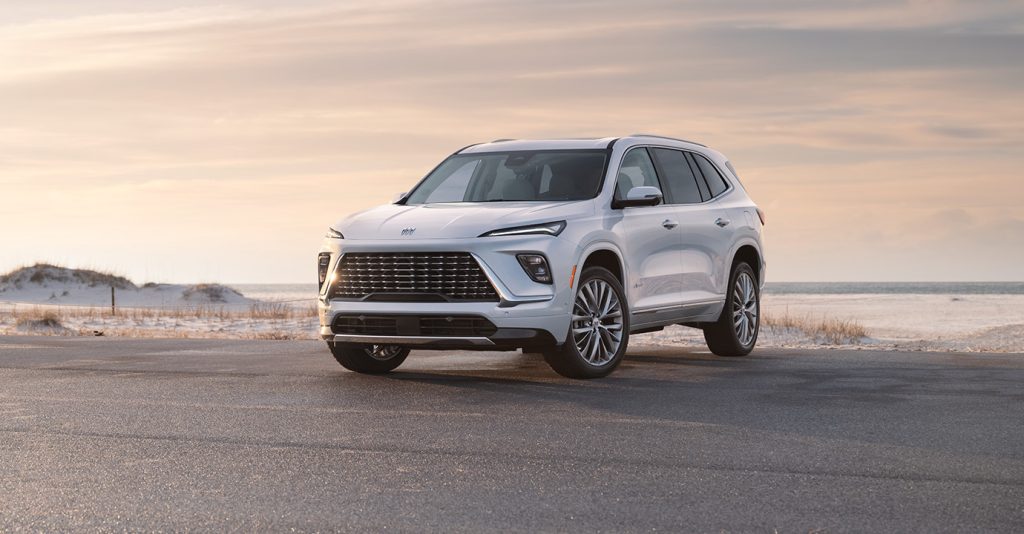 A white SUV parked on a coastal road at sunset.