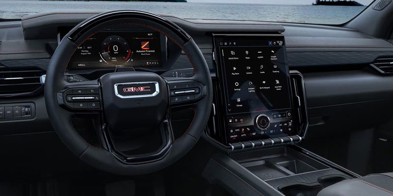 Interior dashboard view of a GMC vehicle featuring a multi-function steering wheel and a large vertical touchscreen display.