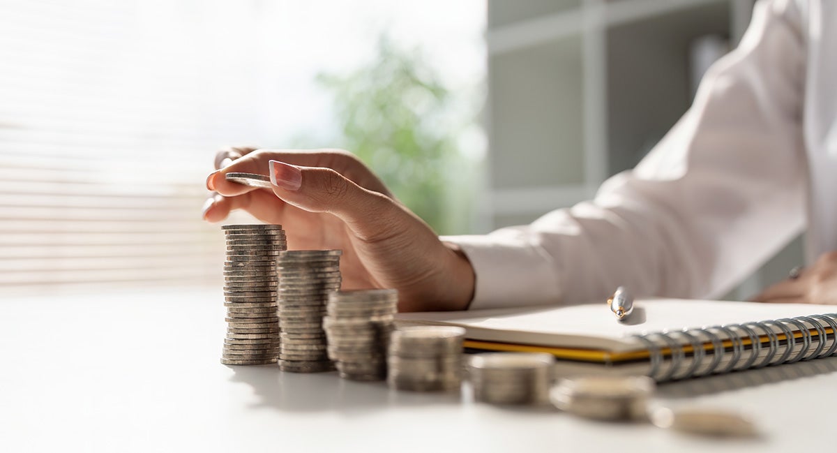 Short Alt Text A person stacking silver coins into ascending columns next to an open notebook on a desk.